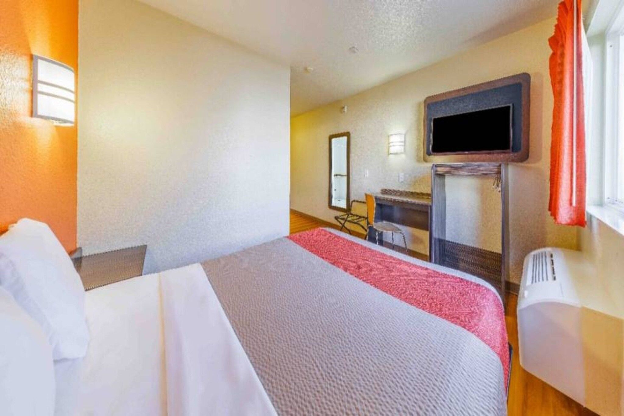 A hotel room with a bed, a desk, a chair, a television, and a window with curtains.