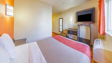 A hotel room with a bed, a desk, a chair, a television, and a window with curtains.