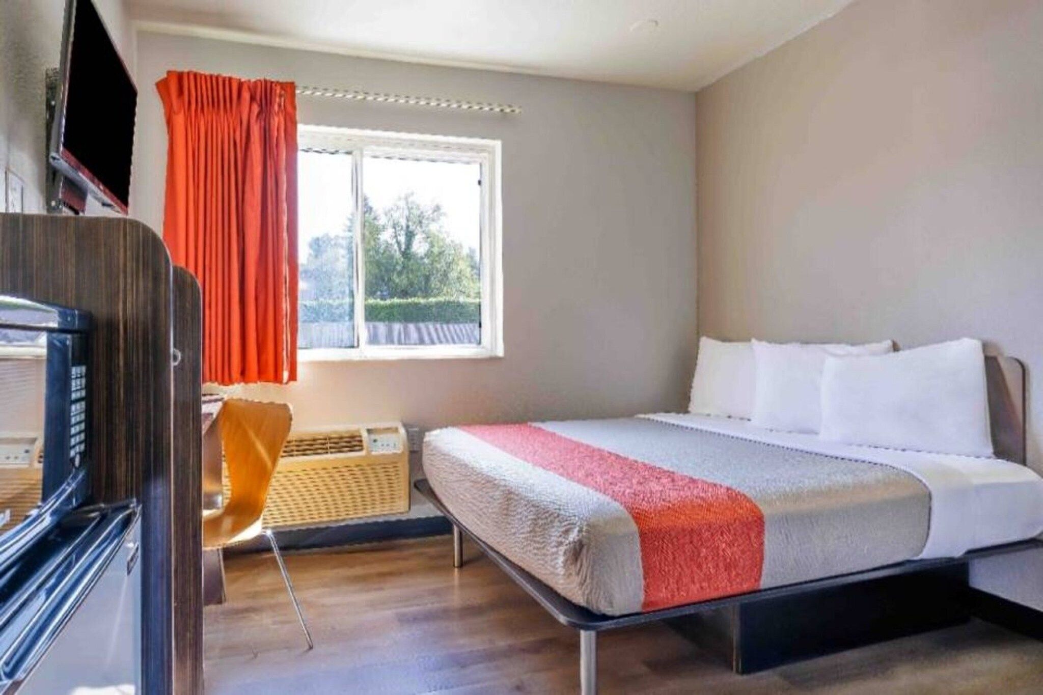 A hotel room with a bed, a desk, a chair, a window, and a television.