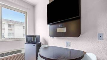 A small room with a flat-screen TV mounted on the wall, a microwave, a small refrigerator, and a round table with two chairs.