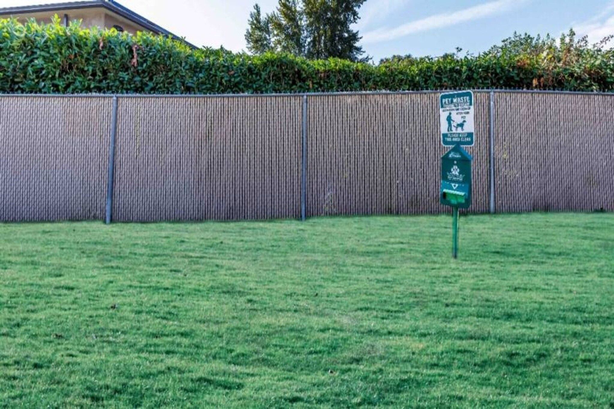 A fenced yard with a pet waste disposal bin and a sign indicating the area is clean.
