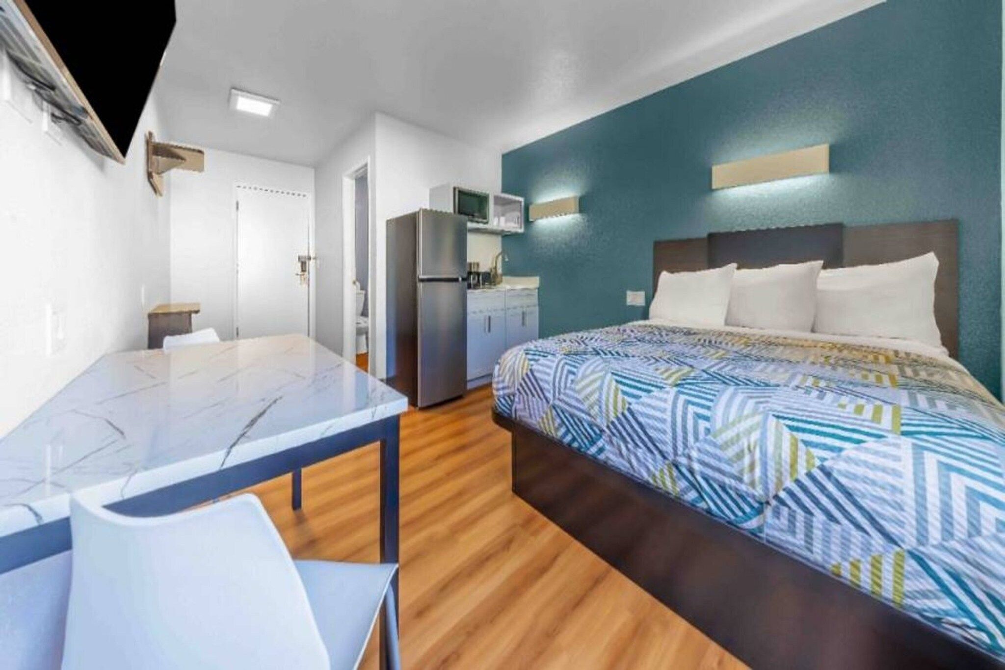 A compact hotel room with a bed, a small kitchenette, a dining table, and a bathroom.
