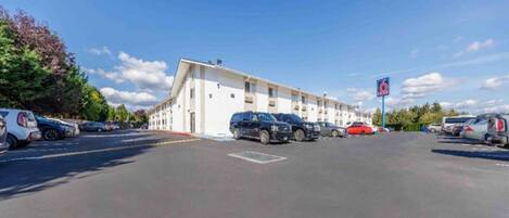 Un motel con una hilera de habitaciones, un estacionamiento y un cielo despejado.