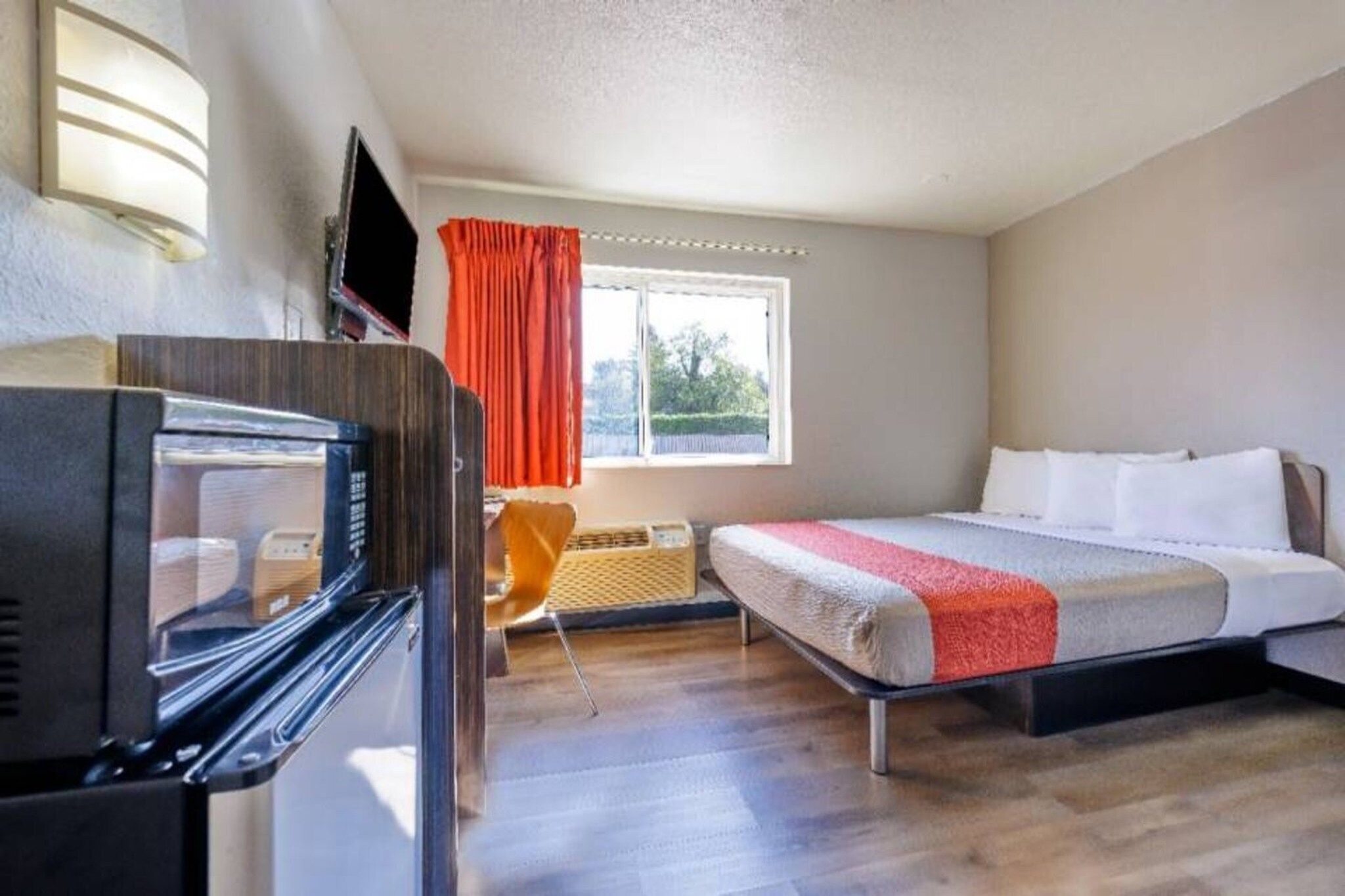 A hotel room with a bed, a TV, a window with curtains, and a microwave.