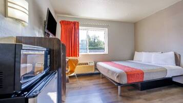 A hotel room with a bed, a TV, a window with curtains, and a microwave.