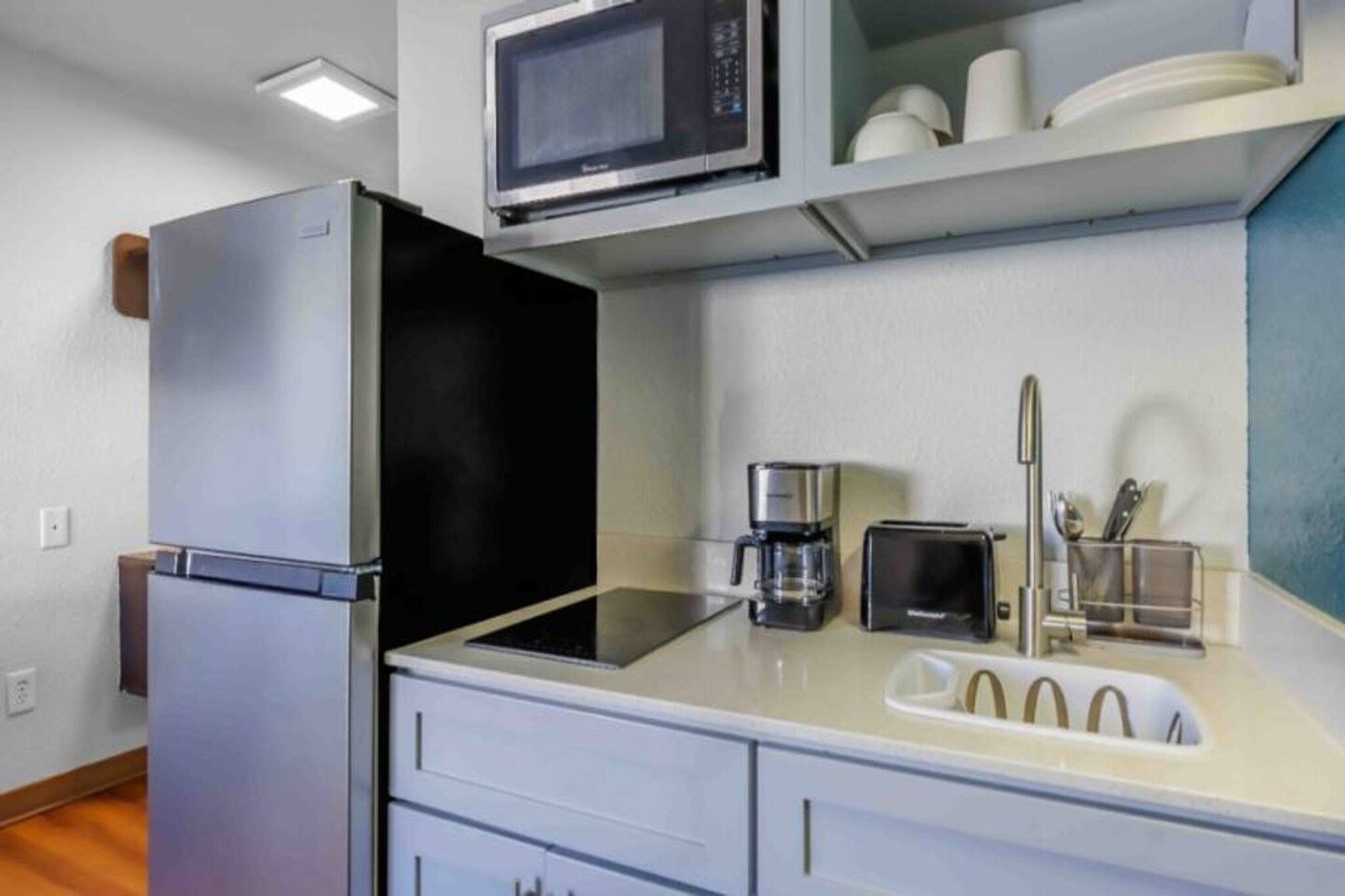 A compact kitchenette with a refrigerator, microwave, coffee maker, toaster, and a sink.
