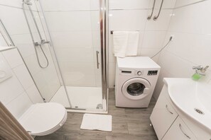 Ein kleines Badezimmer mit Duschkabine aus Glas, Waschmaschine und Toilette.