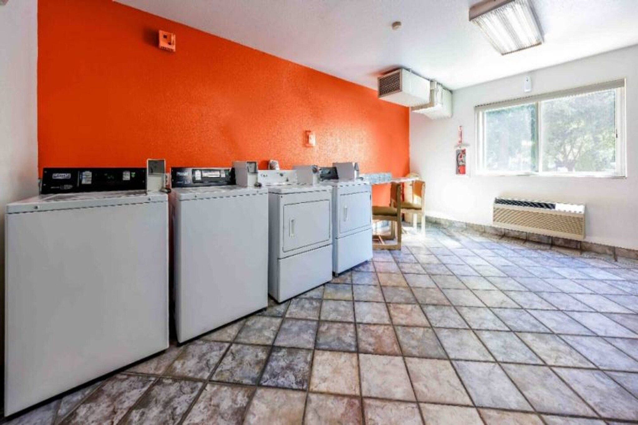 Pesuhuone, jossa on useita pesukoneita, laatoitettu lattia ja ikkuna, josta tulee luonnonvaloa.