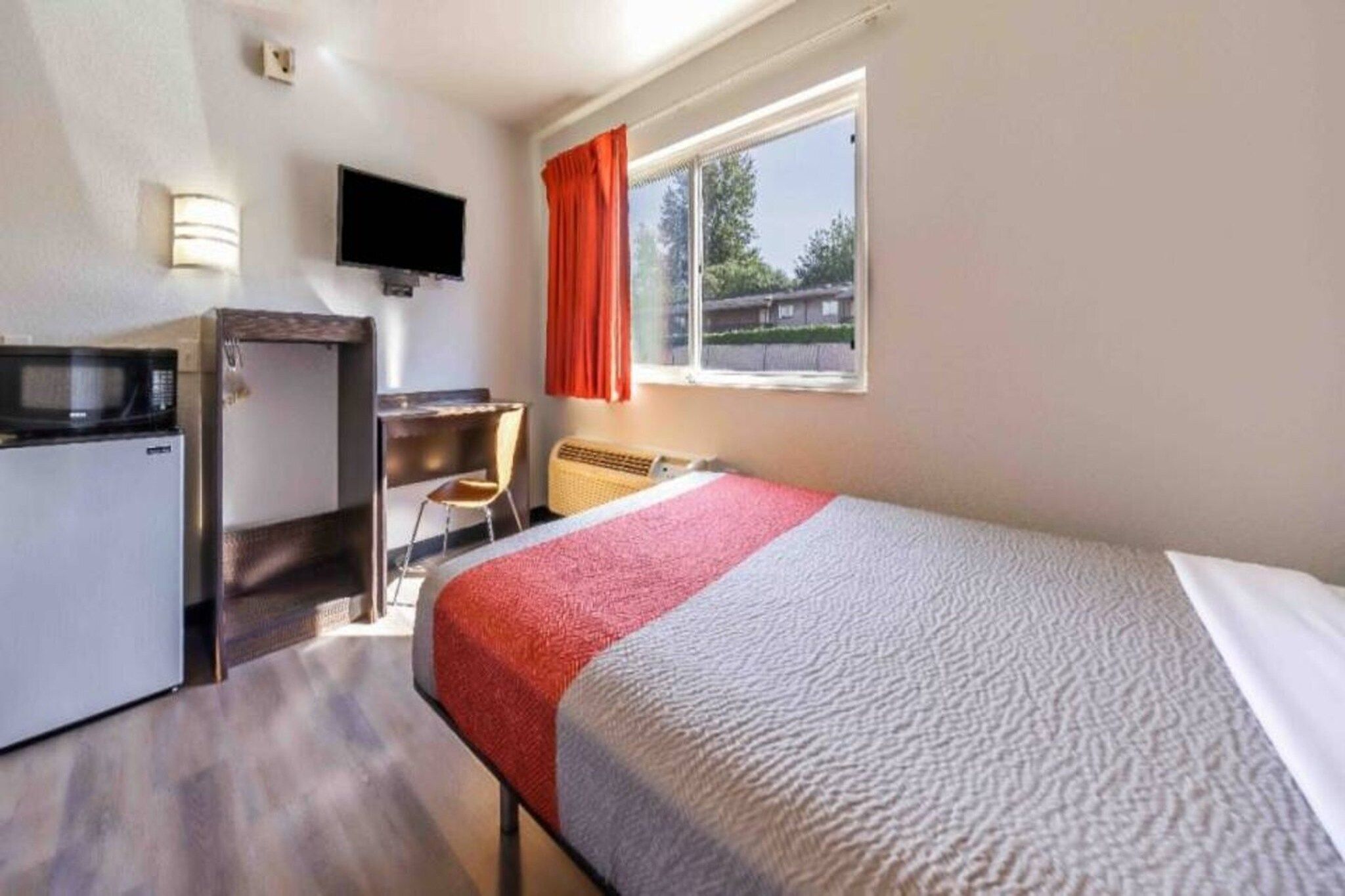 A hotel room with a bed, a desk, a chair, a television, and a window with curtains.