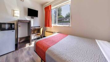 A hotel room with a bed, a desk, a chair, a television, and a window with curtains.