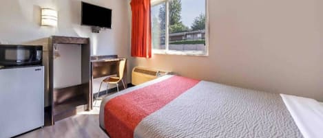 Habitación de hotel con cama, escritorio, silla, televisor y ventana con cortinas.
