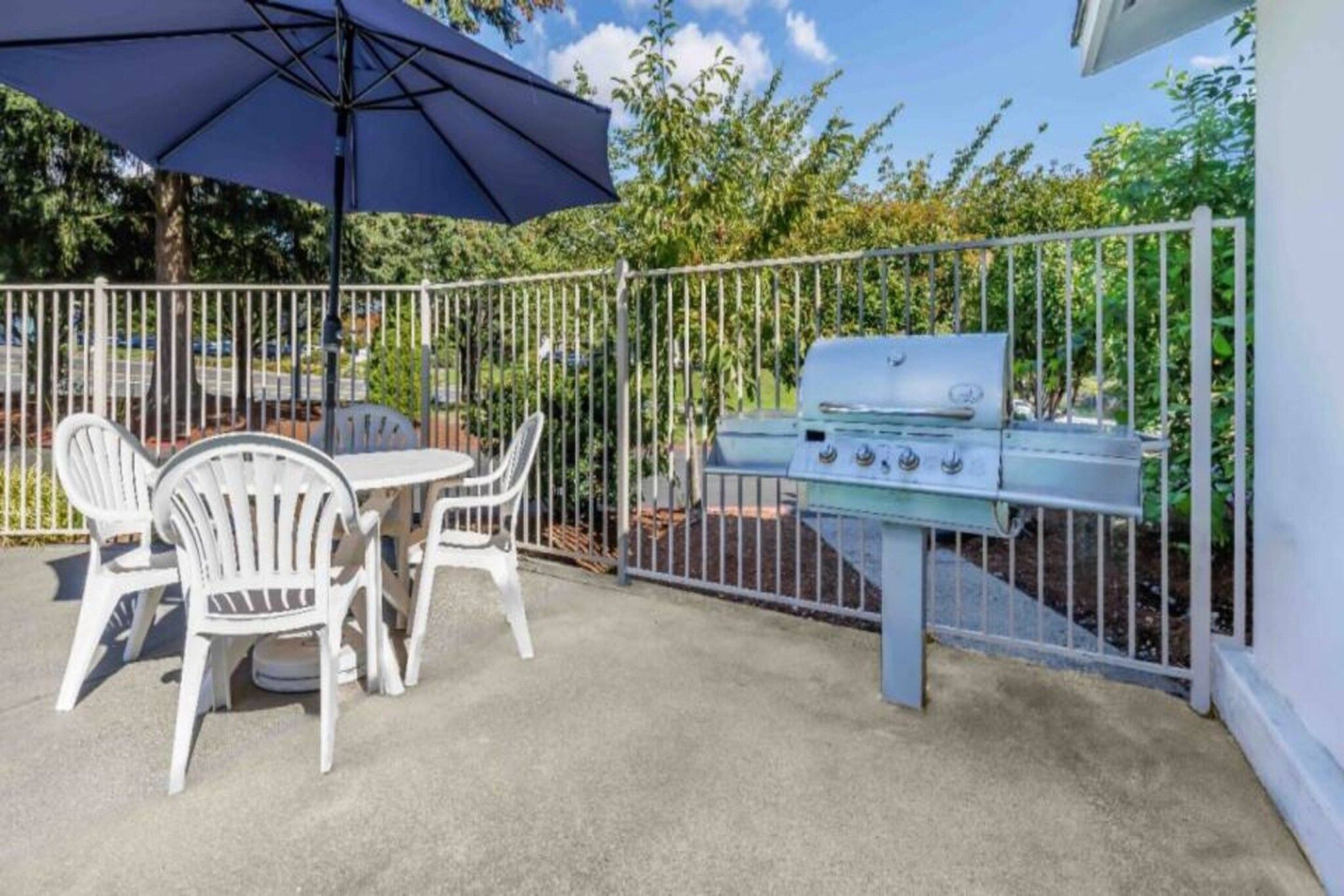 An outdoor patio with a grill, white plastic chairs, and a table.