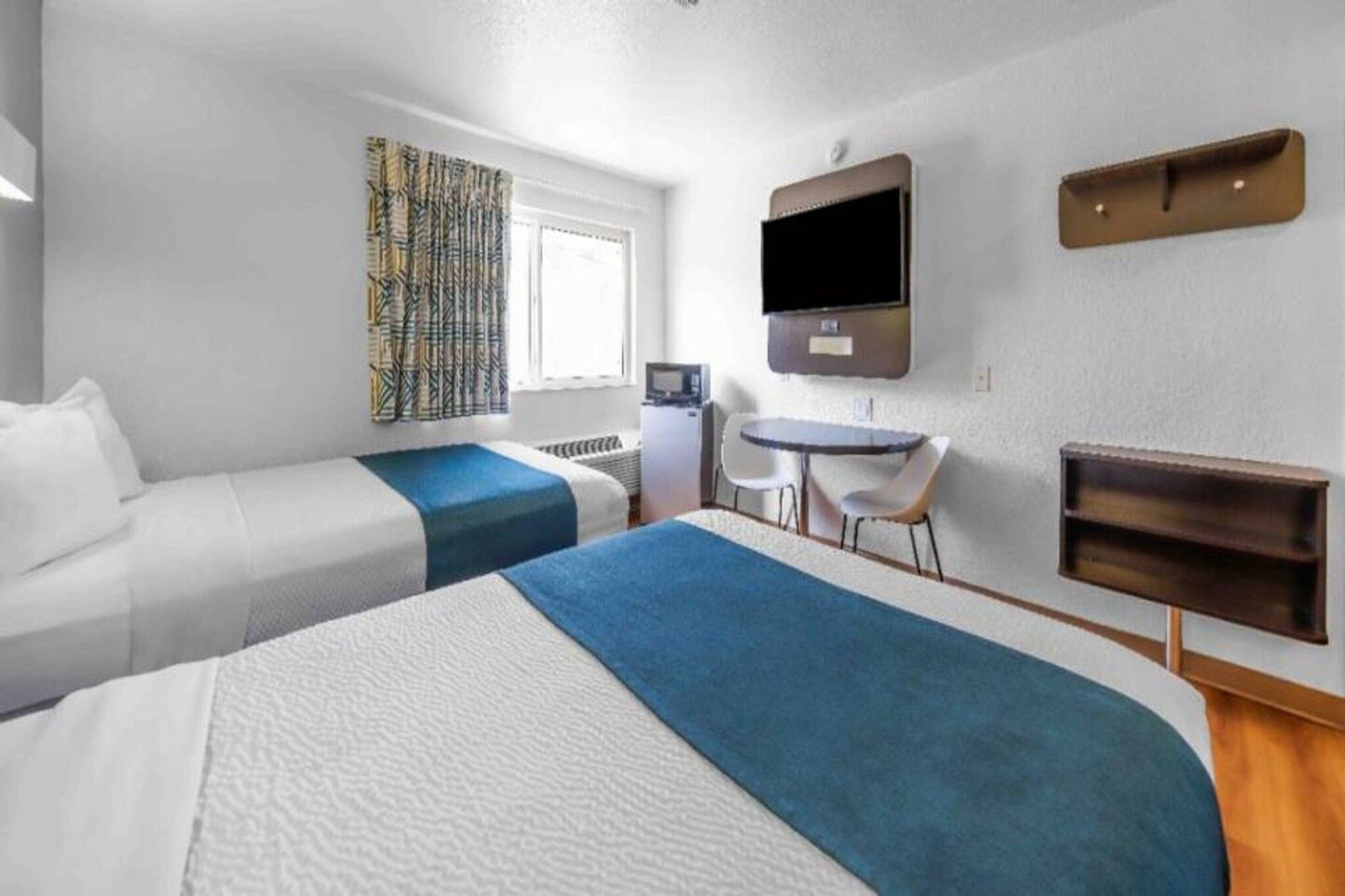 A hotel room with two beds, a desk, a chair, a television, and a small table.