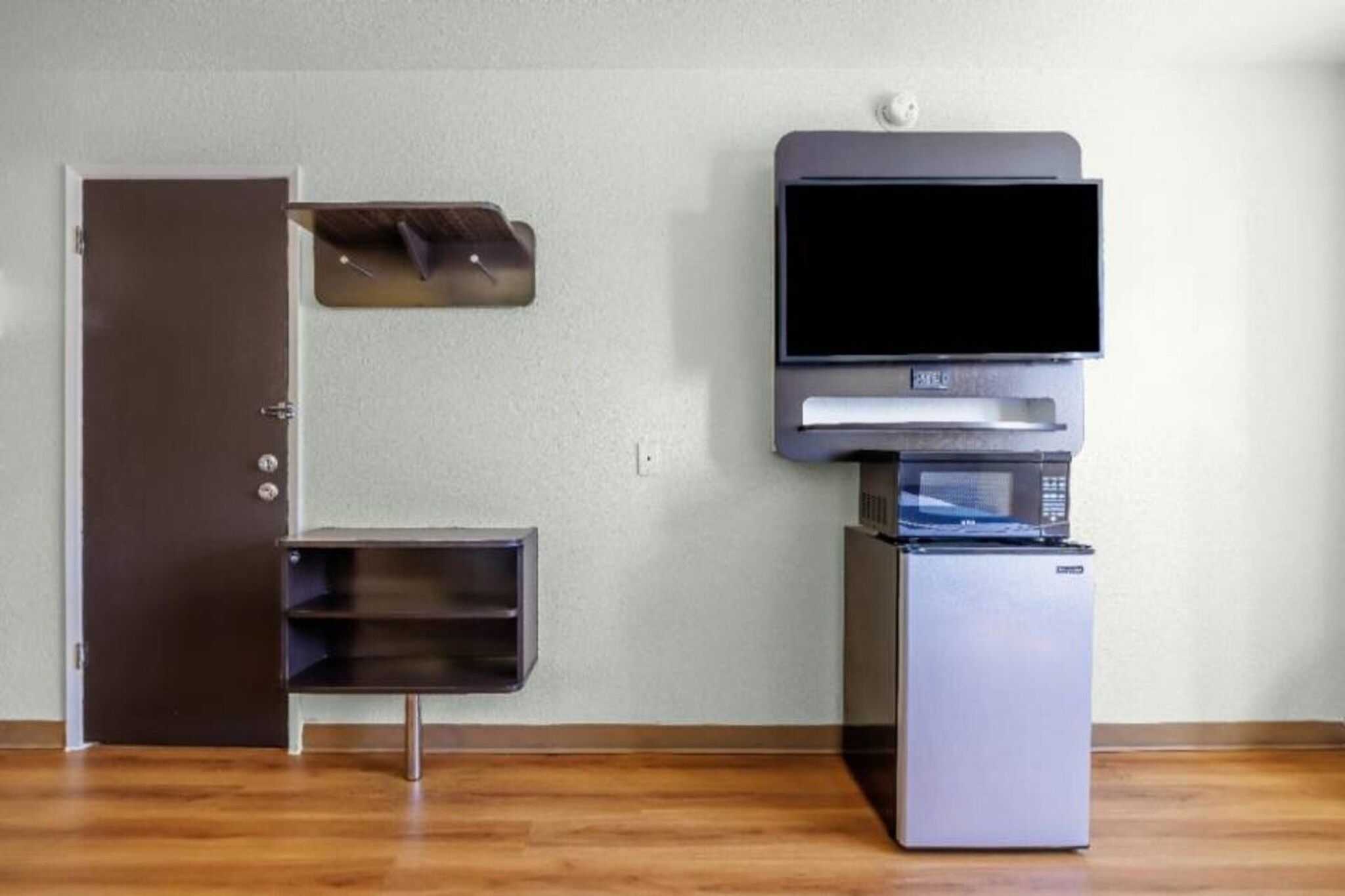 A room with a closed door, a small cabinet, a microwave, and a refrigerator.