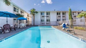 A swimming pool with lounge chairs and umbrellas, surrounded by a fence and a building with multiple windows. - 2 Full Beds | Non-Smoking, Micfridge (Seattle)