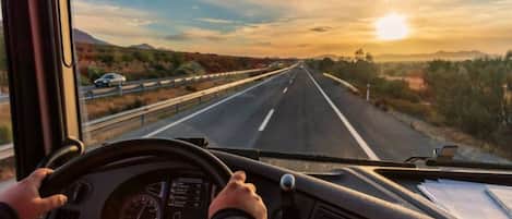 A driver's perspective inside a vehicle on a highway with a clear sky and distant mountains.