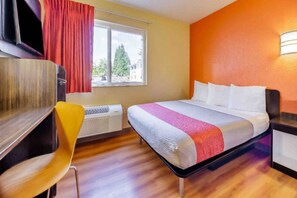 A hotel room with a bed, a desk, a chair, a window with curtains, and an air conditioning unit. - 1 Queen Bed | Non-Smoking, Micfridge (Seattle)