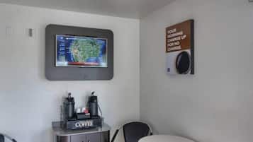 A room with a coffee station, a television mounted on the wall, and a sign about morning coffee.