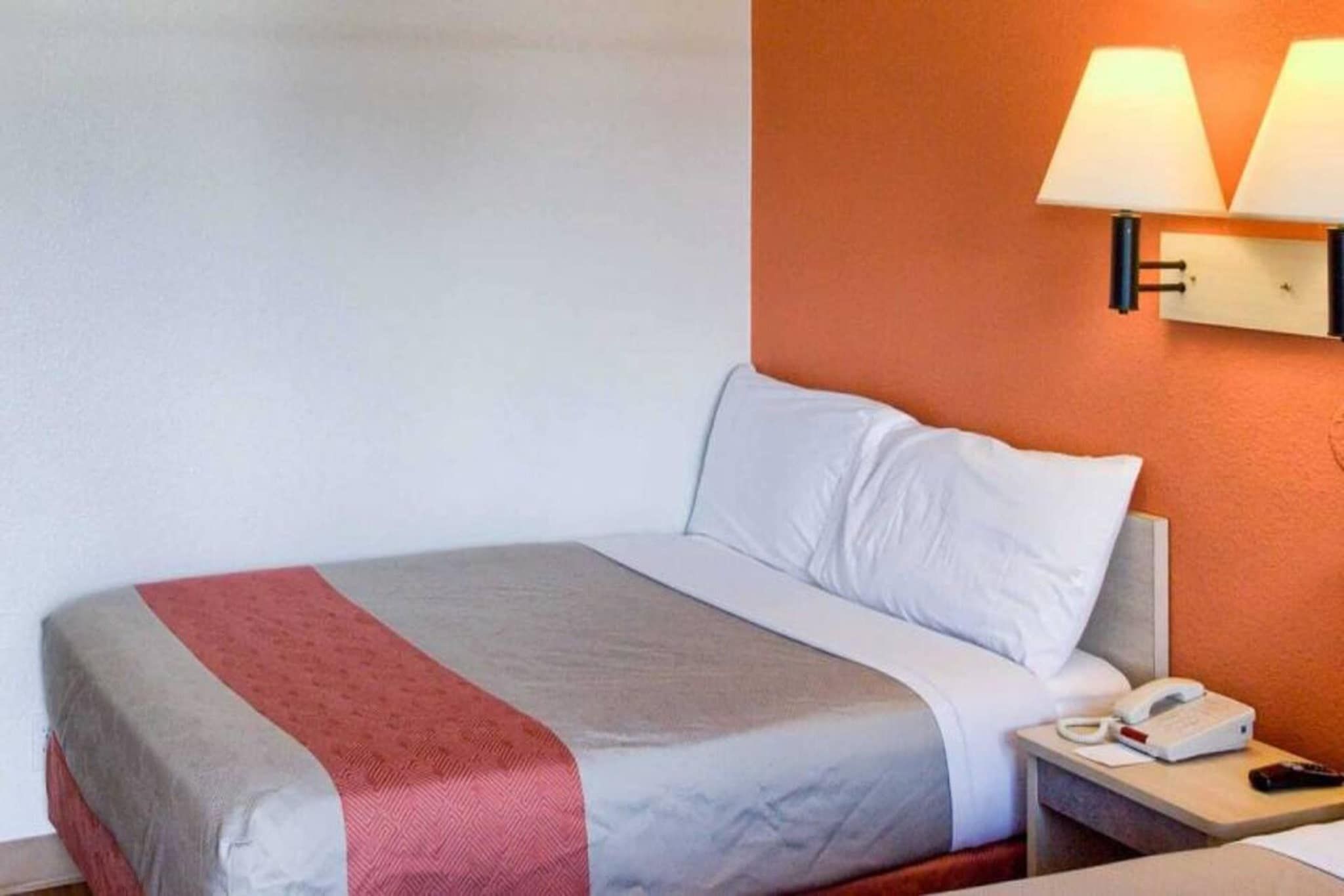 A hotel room with a bed, a nightstand, a lamp, and a phone.
