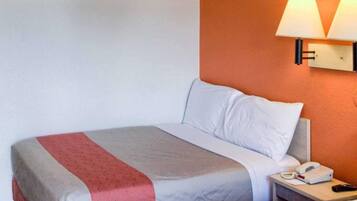 A hotel room with a bed, a nightstand, a lamp, and a phone.