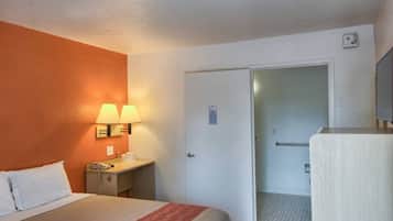 Een hotelkamer met een bed, nachtlampjes, een bureau met telefoon en een deur naar de badkamer.