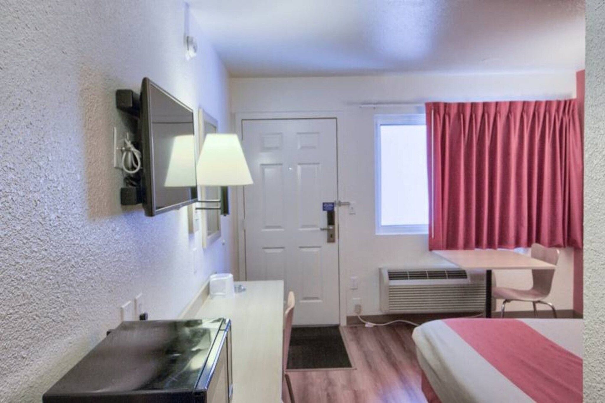 Una camera d'albergo con un letto, una scrivania, una sedia, un televisore e una finestra con tende.