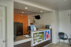 A reception desk with a sign indicating room number 6, a telephone, a computer, and a chair to the right. - 1 Queen Bed | Micfridge (Everett)