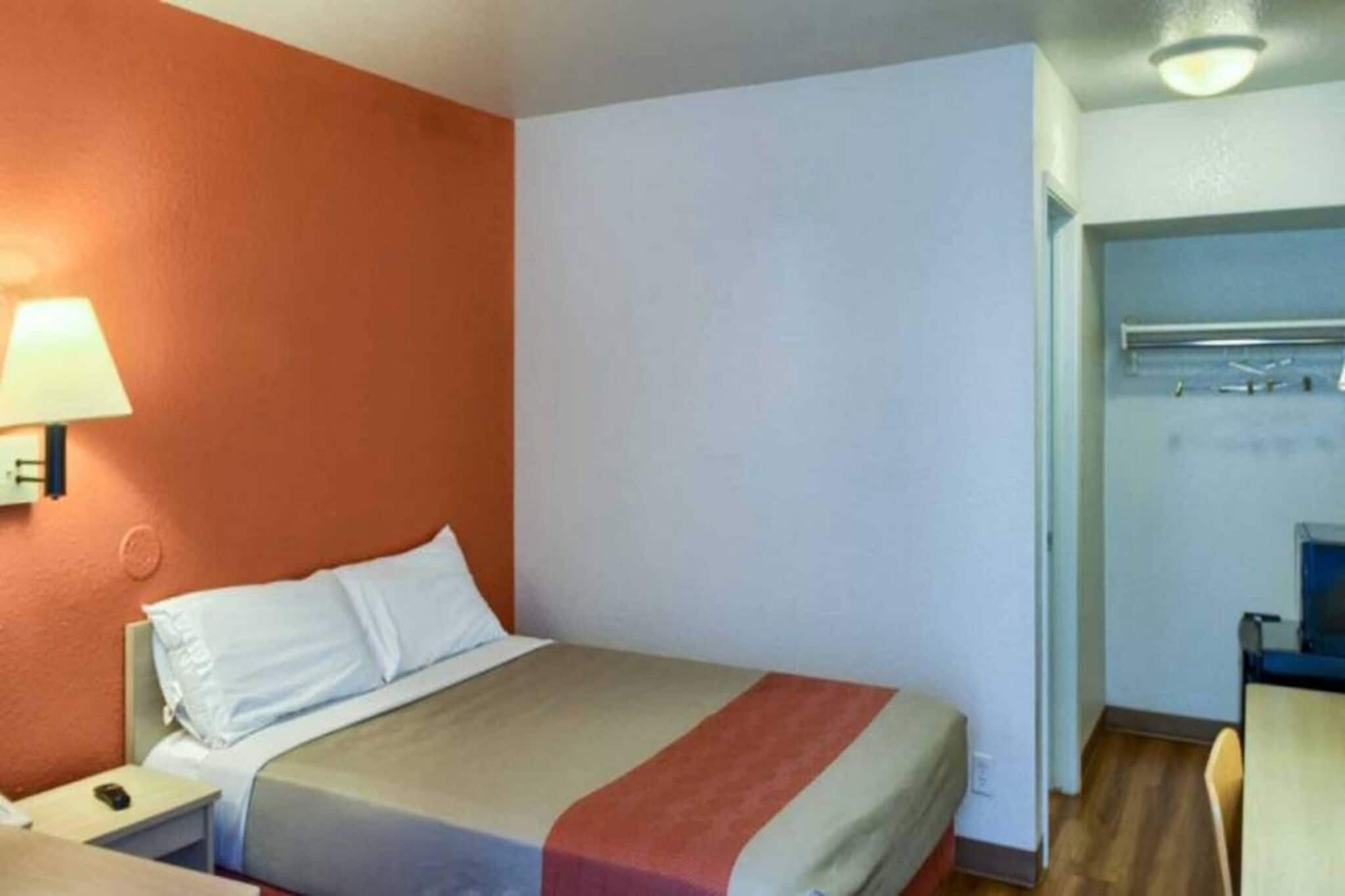 Una camera d'albergo con un letto, un comodino, una lampada e una scrivania con una sedia.
