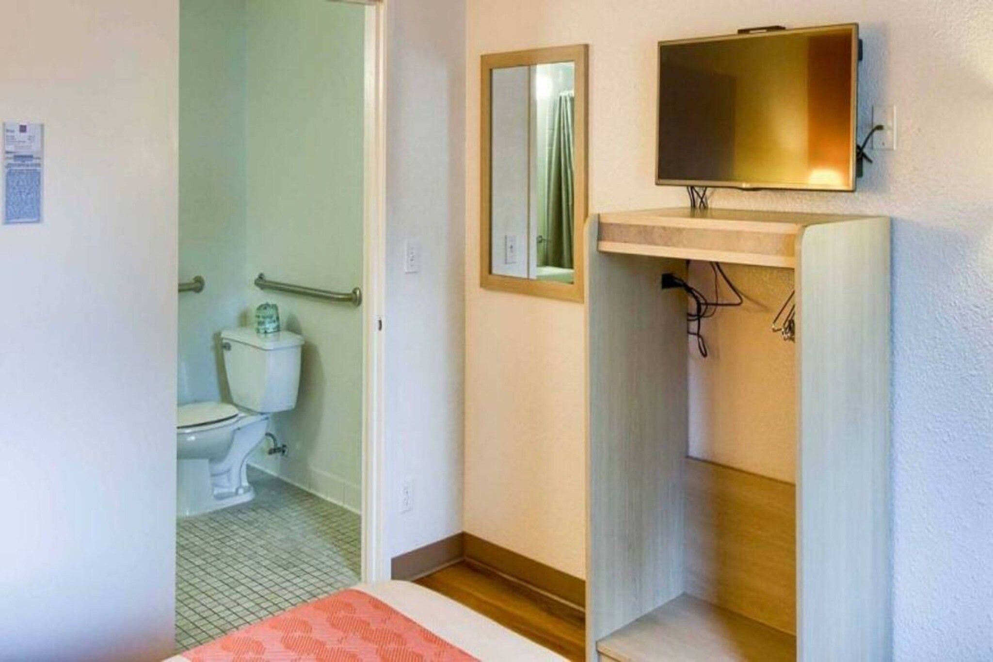 Une salle de bain équipée de toilettes, d’un miroir et d’un lavabo, avec un téléviseur fixé au-dessus.