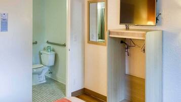 A bathroom with a toilet, a mirror, and a sink with a television mounted above it.
