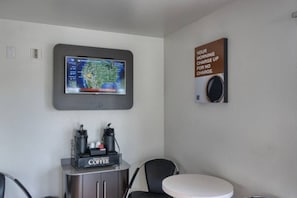 Una stanza con angolo caffè, una TV a parete che mostra una mappa del tempo e un poster motivazionale.