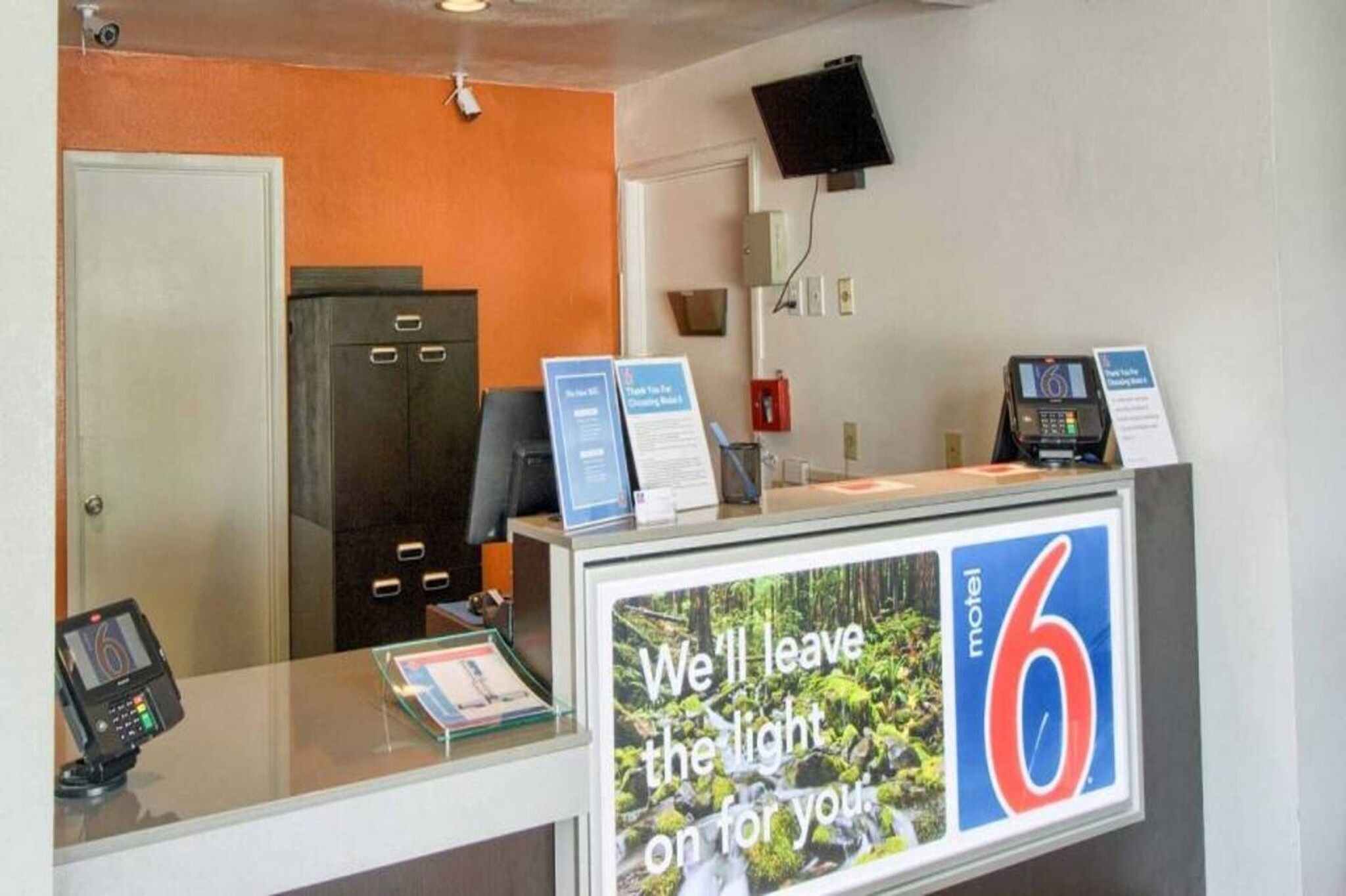 Una mesa de recepción con un cartel que dice 'Dejamos la luz encendida para ti' y el número '6' que indica el motel.