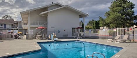 A swimming pool with a diving board, surrounded by a fenced area with lounge chairs and umbrellas.