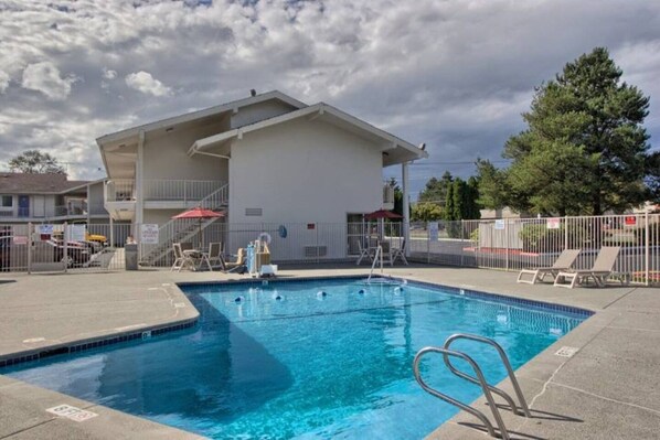 A swimming pool with a diving board, surrounded by a fenced area with lounge chairs and umbrellas.
