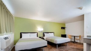 Habitación de hotel con dos camas, un escritorio, una silla y una pequeña cocina.