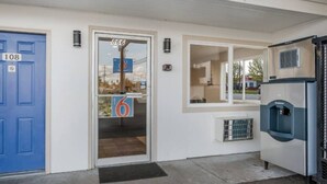 Entrada de un edificio con una puerta azul identificada con el número '108', una puerta de vidrio con el número '866', y un dispensador de agua a la derecha.