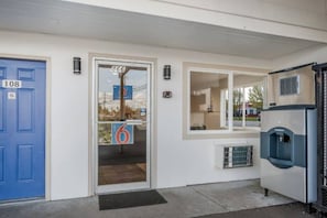 Entrada de edifício com porta azul identificada com o número '108', porta de vidro com o número '866' e um bebedouro à direita.