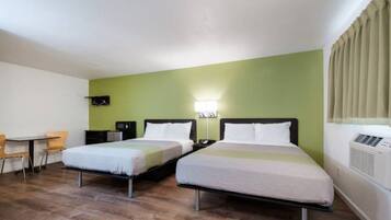 A hotel room with two beds, a desk, a chair, a wall-mounted TV, and an air conditioning unit.