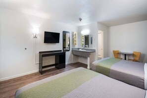 Una habitación de hotel con cama, escritorio, televisor, espejo y baño.