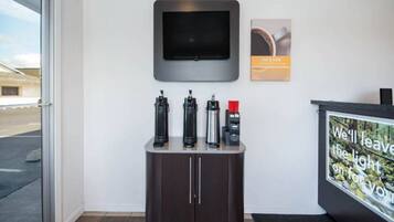 A reception area with a flat-screen TV mounted on the wall, a coffee machine, and a water dispenser on a counter.