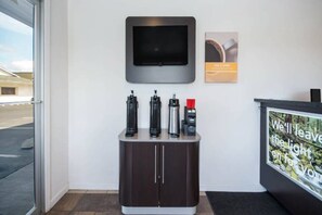 Zona de recepción con un televisor de pantalla plana en la pared, una cafetera y un dispensador de agua sobre un mostrador.