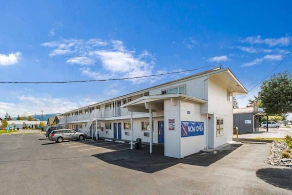 Um motel com estrutura de dois andares, área de estacionamento coberta e uma placa indicando que está aberto.