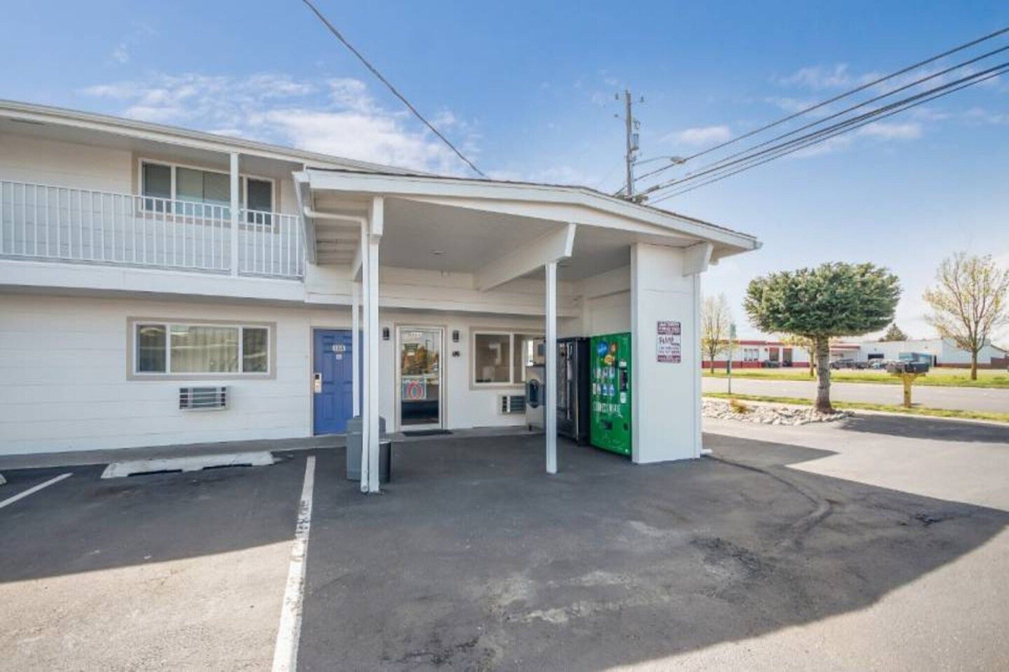 Un motel amb entrada coberta, una porta blava i una màquina expenedora verda.