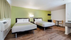Habitación de hotel con dos camas, un escritorio, una silla y una pequeña kitchenette.