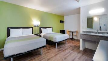 Ein Hotelzimmer mit zwei Betten, einem kleinen Tisch, Stühlen, einem Badezimmer mit Spiegel und einer grünen Wand.