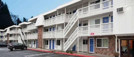 A multi-story motel with a 'NOW OPEN' sign, a parking lot, and a staircase leading to the upper floors.