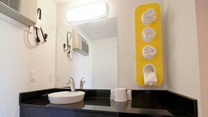 Een moderne badkamer met een zwart aanrecht, een witte wastafel en een spiegel. Handdoeken hangen aan een gele handdoekhouder.