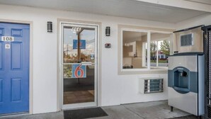 Entrada de un edificio con una puerta azul identificada con el número '108', una puerta de vidrio con el número '866' y un dispensador de agua azul a la derecha.