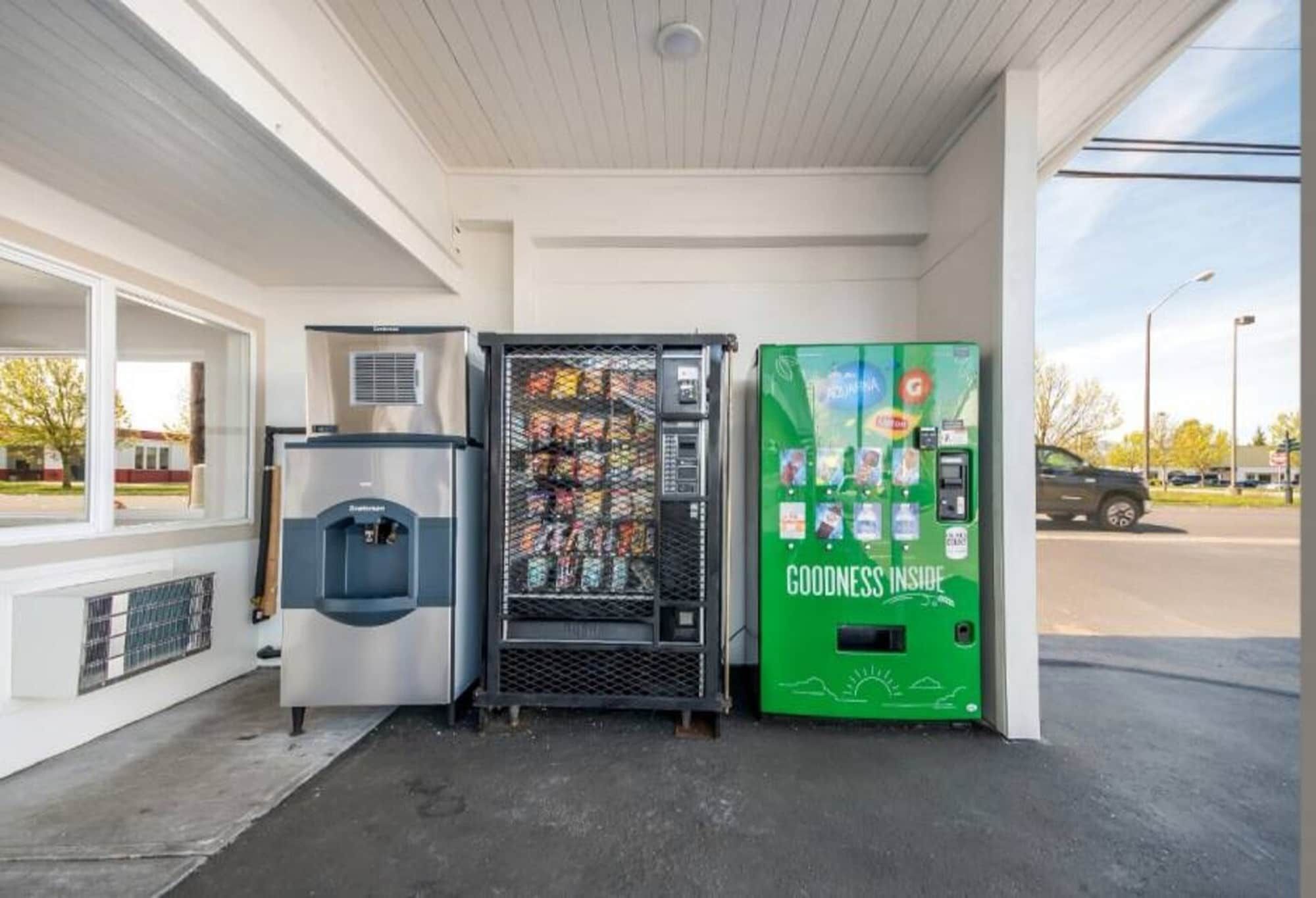 Une station-service équipée d’un distributeur de carburant en libre-service, d’un distributeur automatique de boissons réfrigérées et d’un distributeur automatique vert.