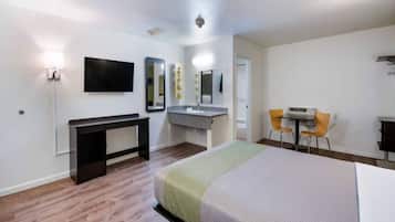 A hotel room with a bed, a desk, a chair, a TV, and a bathroom with a mirror and sink.